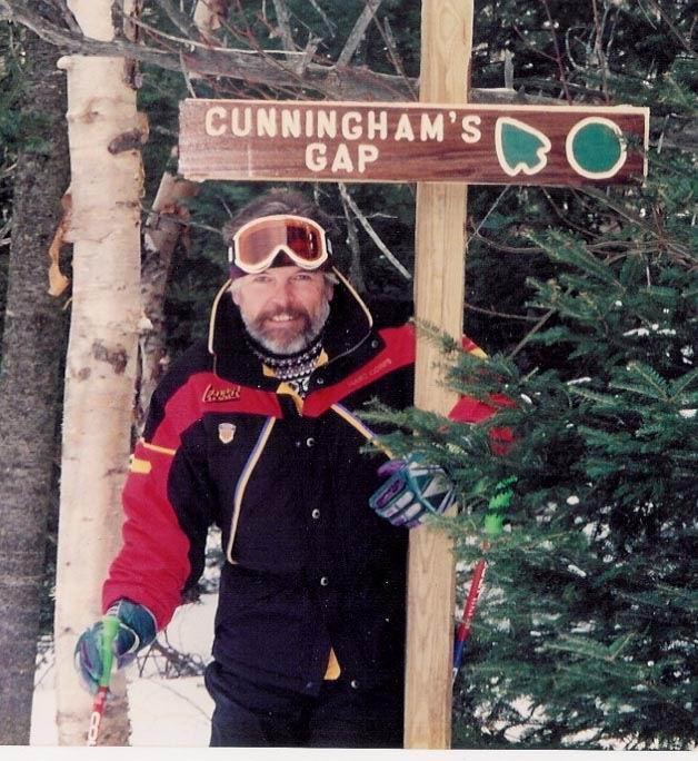 Bill Cunningham stands by a trail sign after his own name.
